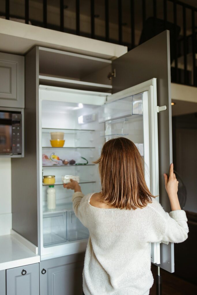 A woman reaches into a refrigerator in a contemporary kitchen, creating a lifestyle moment.