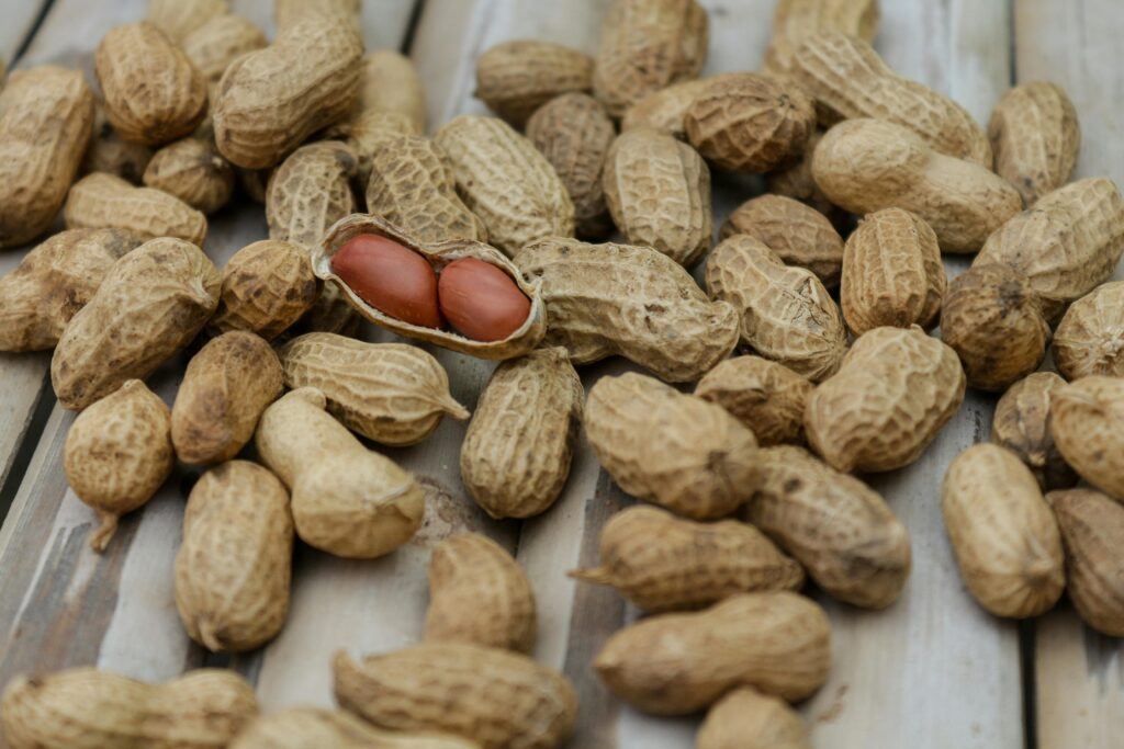 현재 이미지: A detailed close-up of peanuts in their shells scattered on a wooden surface.