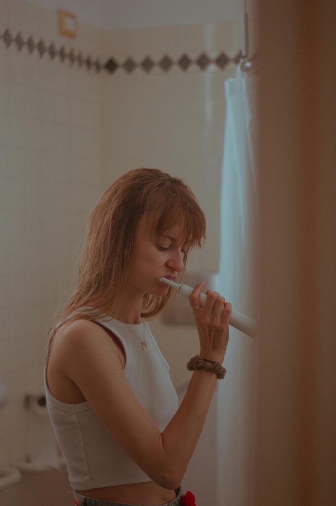 Brunette woman brushing her teeth in a bathroom with a serene expression.
