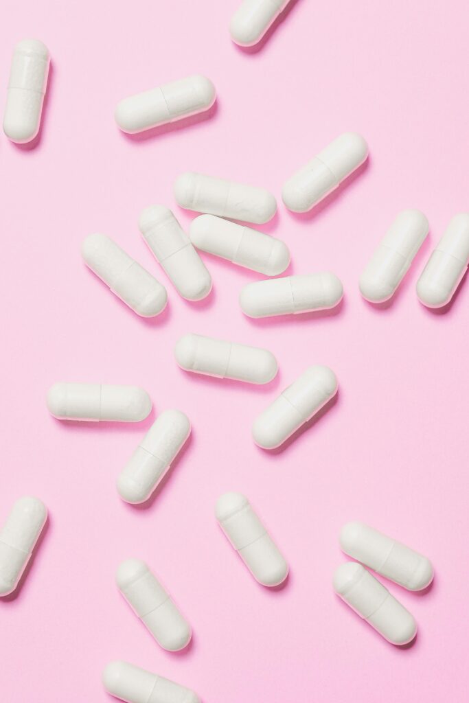 White medicinal capsules scattered on a vibrant pink background, symbolizing healthcare and wellness.