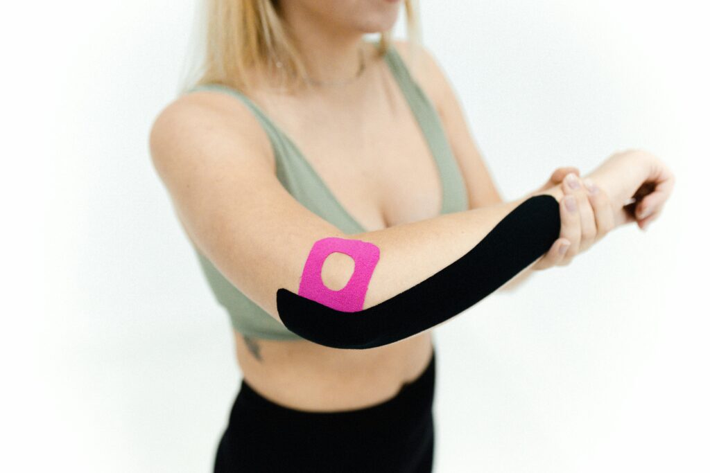 Close-up of a woman applying kinesio tape on her arm for therapeutic treatment on a white background.