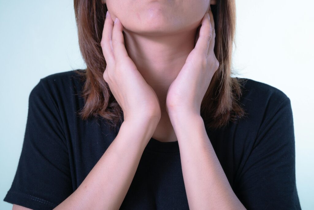 현재 이미지: Close-up of a woman touching her neck, possibly indicating discomfort or throat pain.