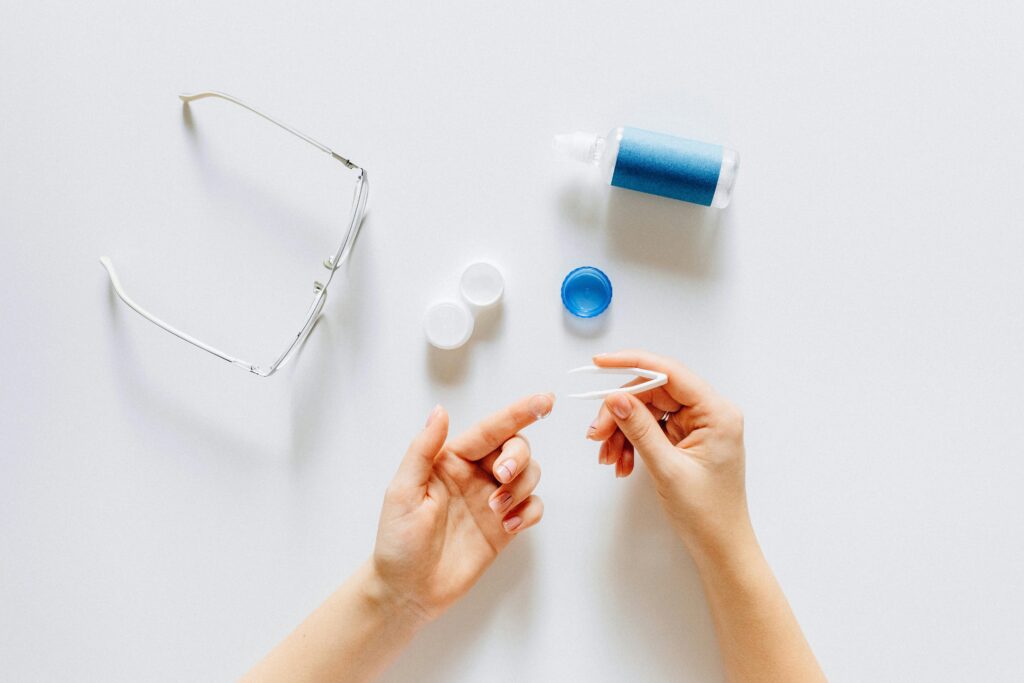 Top view of contact lens tools and glasses on a white surface.